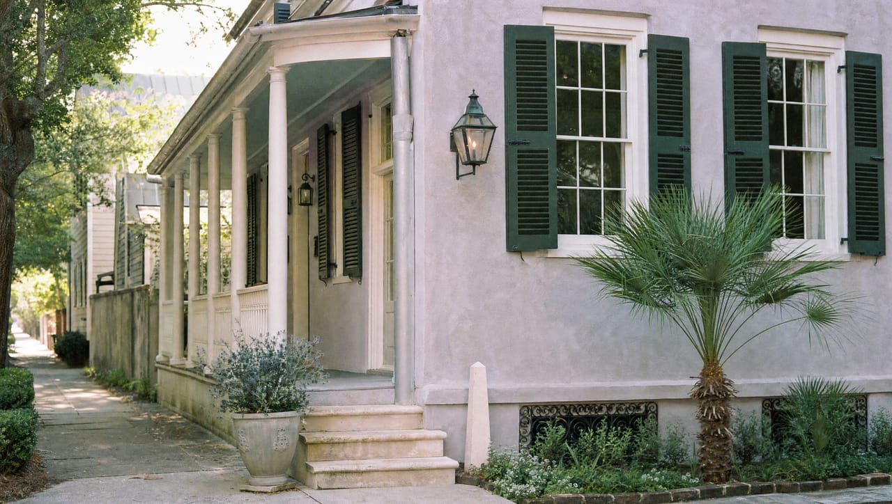 The pale lilac-grey Charleston single house with a side piazza, green shutters and a palmetto